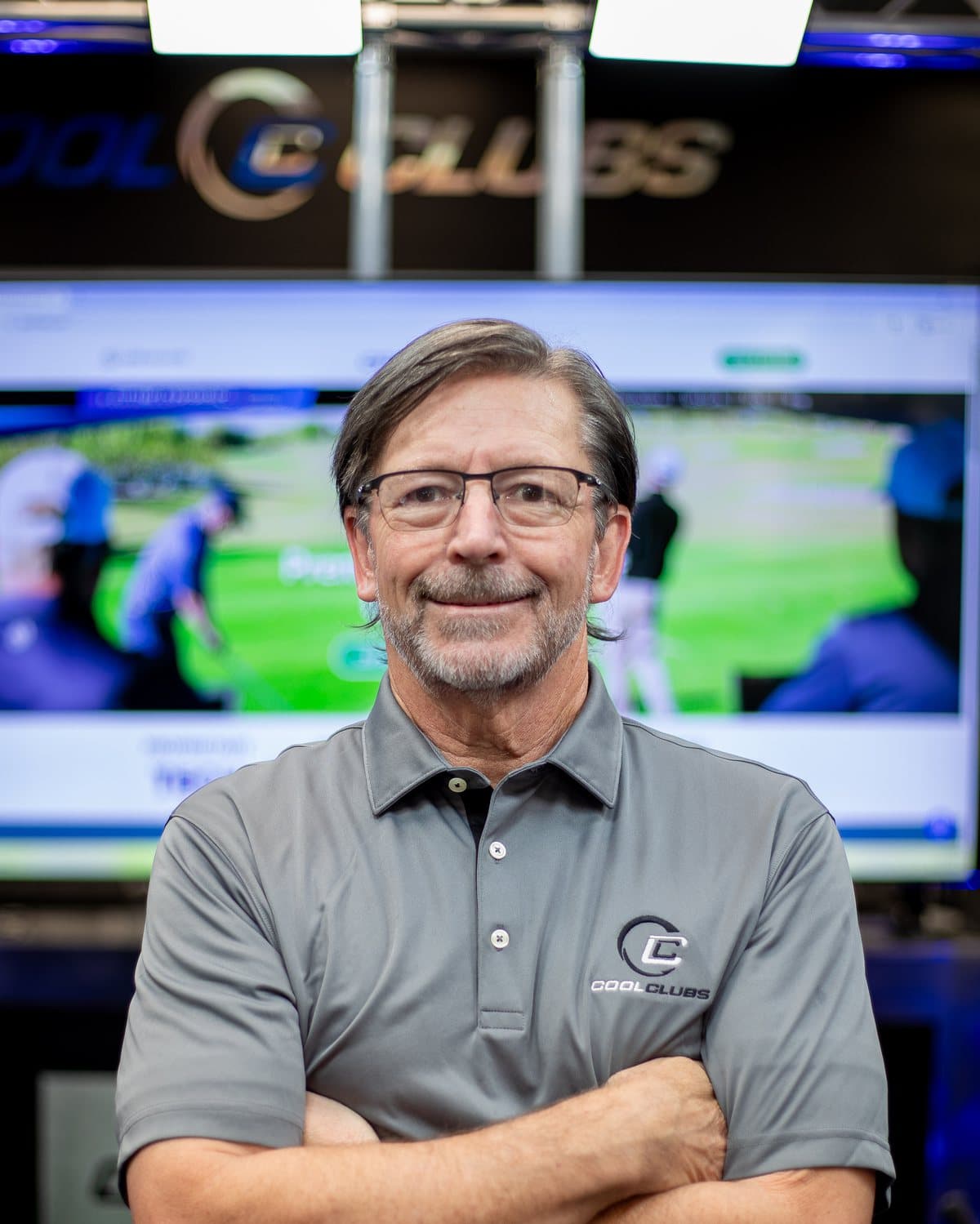 Mark Timms, founder of Cool Clubs, standing with arms crossed in a Cool Clubs fitting bay in front of a simulator screen